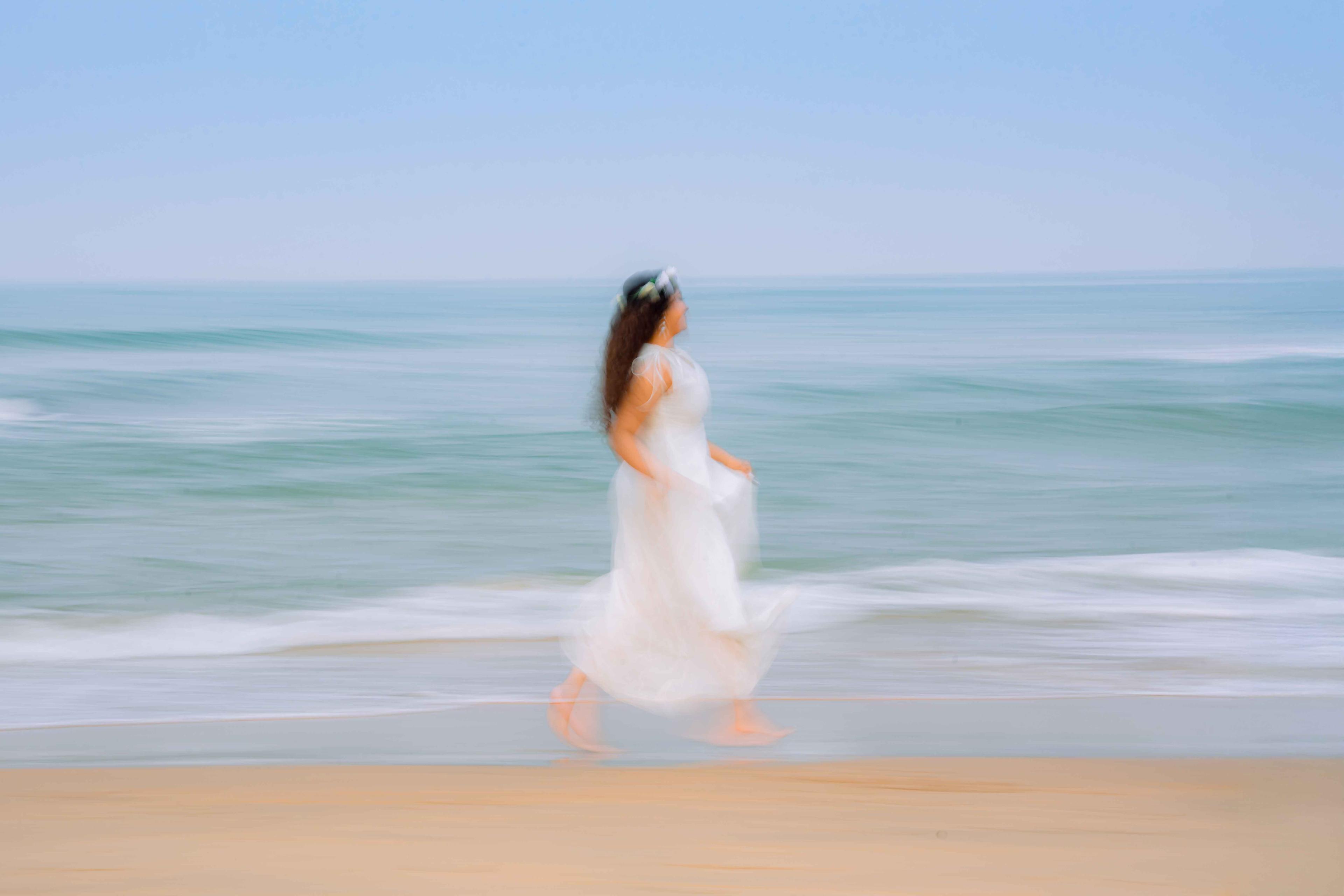 Model in a flowing white dress walking along the shoreline