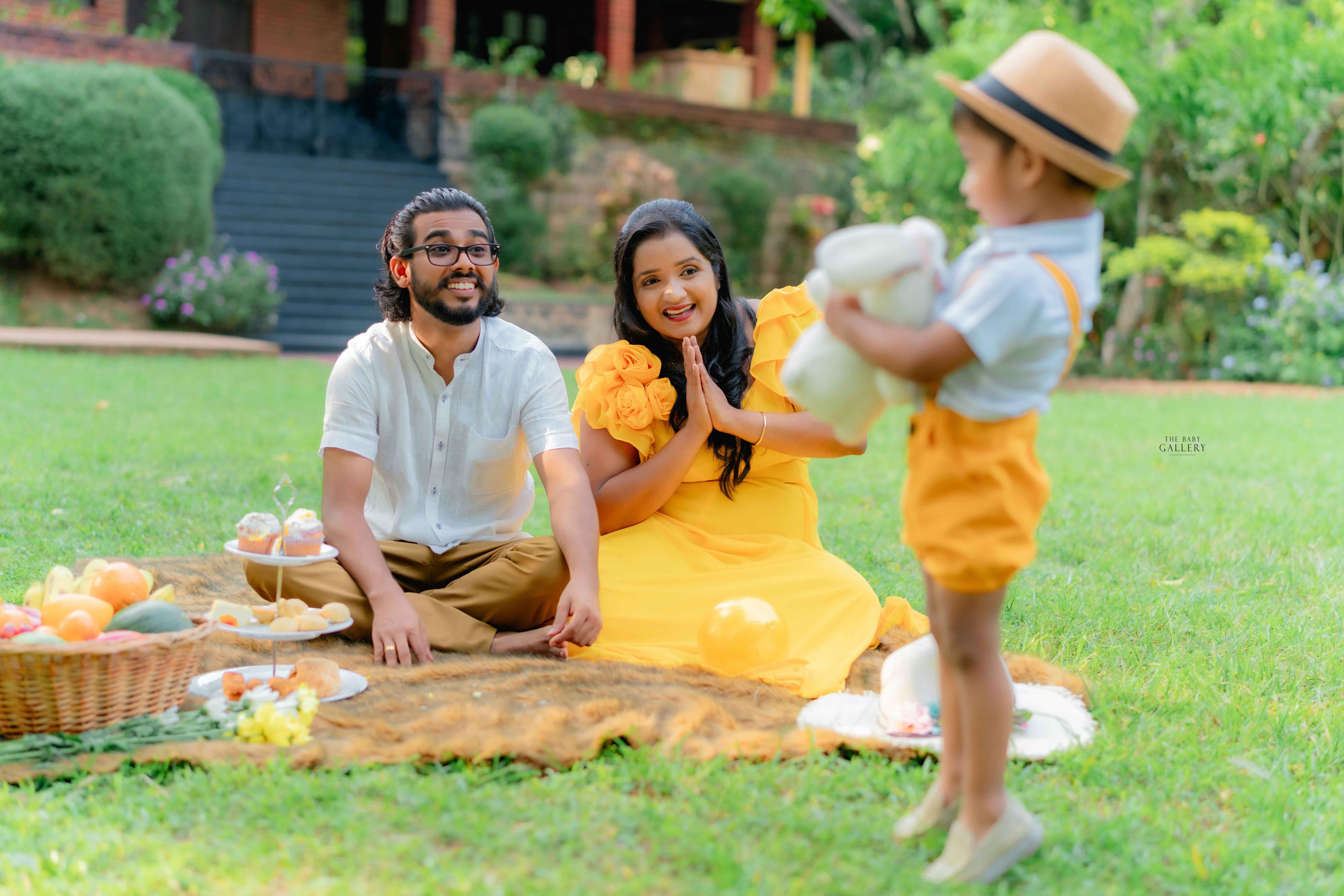 Family picnic on a garden lawn with a toddler in a straw hat