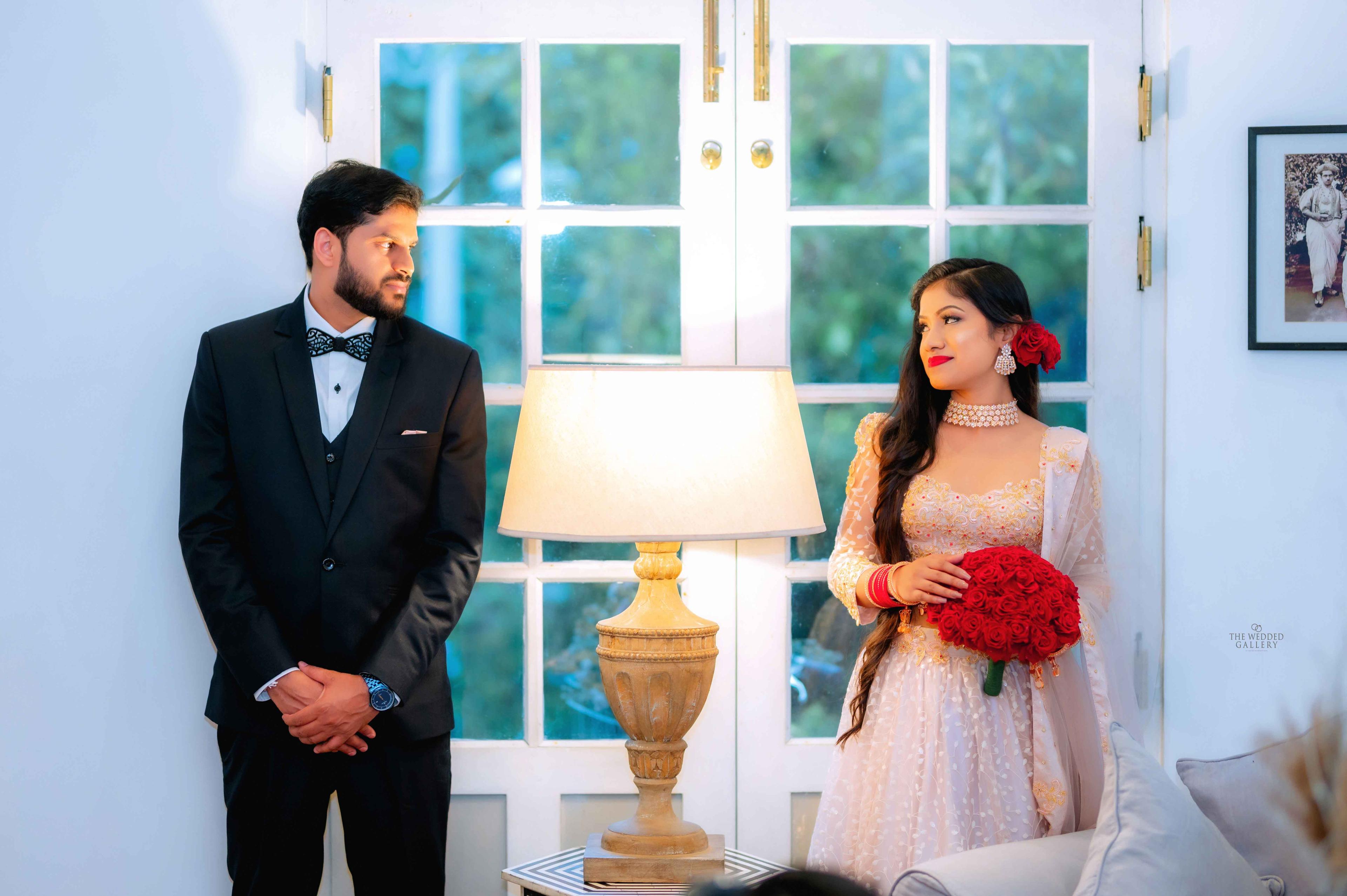 Groom in a tuxedo and bride with a red bouquet in a bright room with a vintage lamp